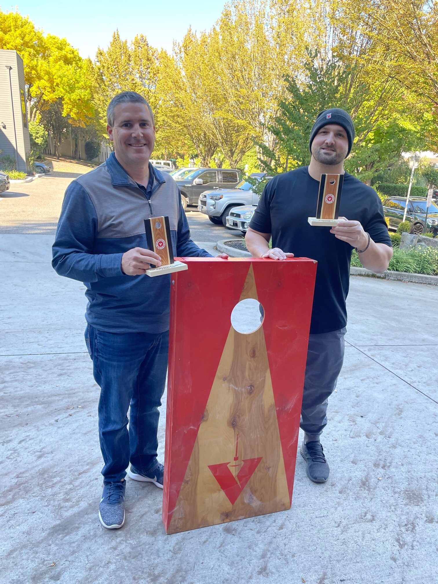 Two VLMK staff holding a cornhole board and trophies